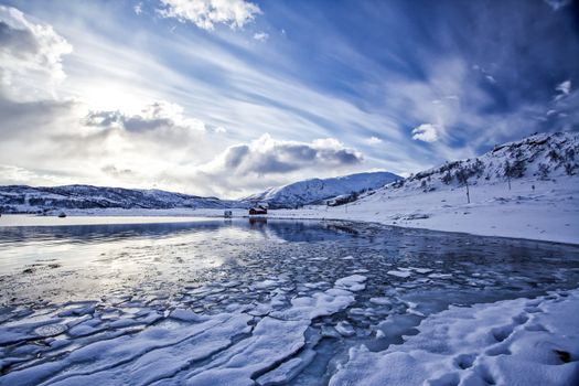 A beach covered by snow in winter time in front of a covered with ice pieces sea