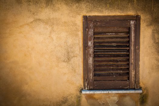 Closed wood window on an ancient yellow house wall