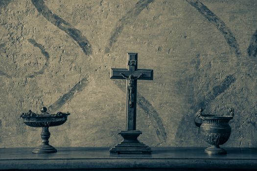 An ancient and weathered crucifix on a wood table between bronze vases