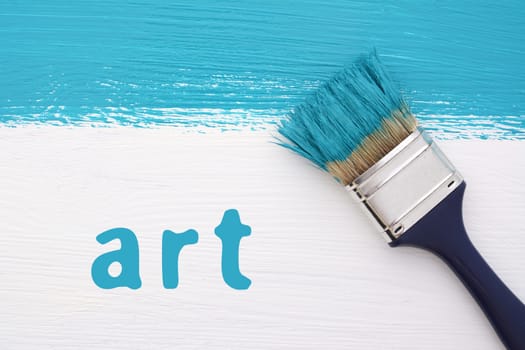 Stripe of turquoise paint with a paintbrush and the word ART on a white wooden board