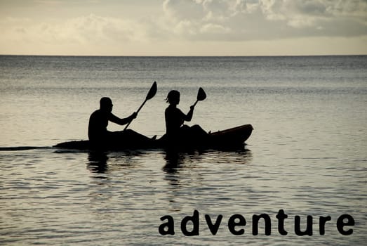 Man and woman silhouetted at sea in a kayak, word ADVENTURE as concept text