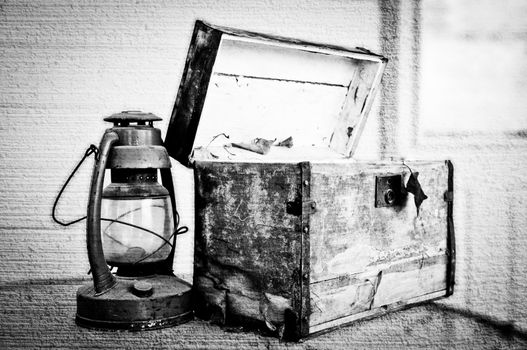 Black and white image of a weathered old chest and lantern