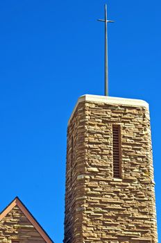 Modern steeple on a christian church made from stones with a cross on the top.