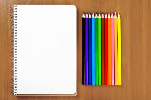 notebook and a set of colored pencils on wooden background