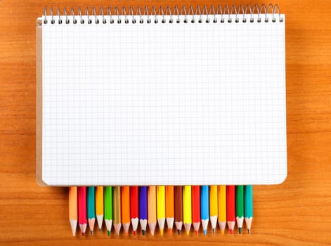 notebook and a set of colored pencils on wooden background