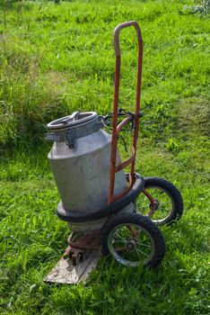 Old aluminum cans on old hand truck on a background of green grass.