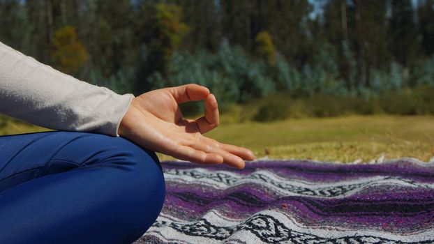 Hand detail of woman sitting doing yoga in the park on a blanket fabric