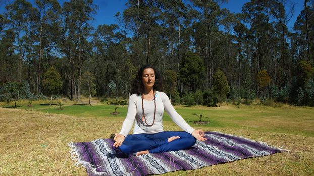 Young latin woman sitting doing yoga in the park on a blanket fabric