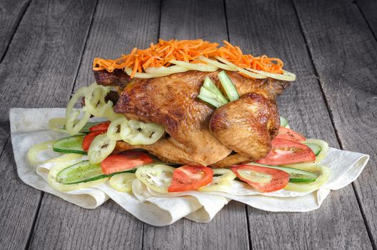 Fried chicken with vegetables lying on the PITA bread, the old wooden background.