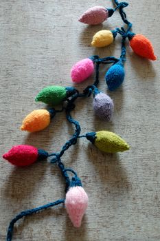 Group of colorful Xmas ornament for winter holiday, handmade product from yarn, knitted Christmas lights bulb on wood background