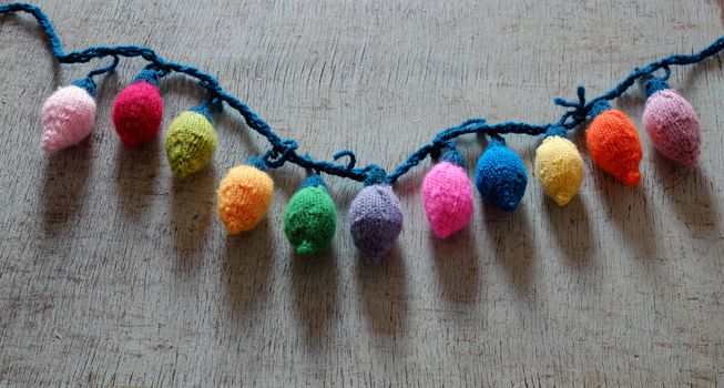 Group of colorful Xmas ornament for winter holiday, handmade product from yarn, knitted Christmas lights bulb on wood background
