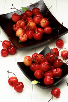 Fresh Ripe Sweet Maraschino Cherries in Two Black Wooden Plates closeup on Plank White background. Focus on Foreground