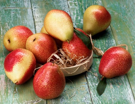 Heap of Ripe Yellow and Red Pears with Leafs in Wicker Bowl closeup on Cracked Wooden background