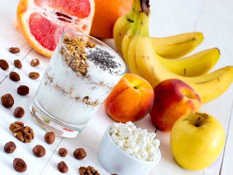 Healthy breakfast: cottage cheese and yogurt with muesli and chia seeds, fruits and nuts on white wooden background. Dieting, healthy lifestyle concept meal