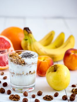 Healthy breakfast: yogurt with muesli and chia seeds, fruits and nuts on white wooden background. Dieting, healthy lifestyle concept meal. Vertical with copyspace