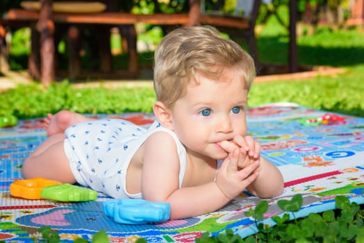 Beautiful baby boy eight month old crawling in the garden with finger in mouth ,close up.