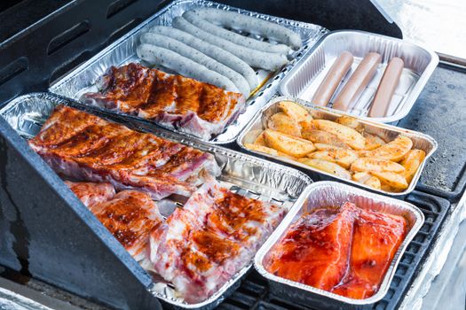 Meat and grill sausages on a gas grill in aluminum dishes