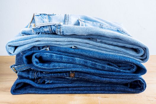 Stack of blue jeans on wooden table.