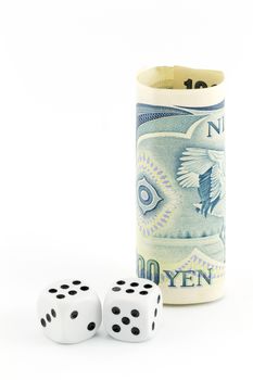Yen currency stands next to pair of dice on white background in vertical image with copy space.  Metaphor reflects concept of challenges and risks in Japan.