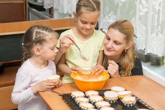 The elder daughter pours batter for cakes in tins, under the care of my mother and younger sister