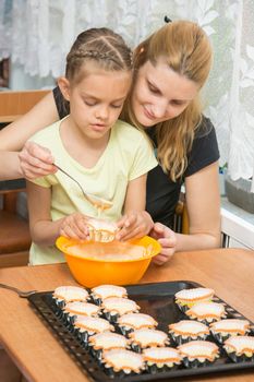 Mother helps daughter to pour batter into the mold for cupcakes