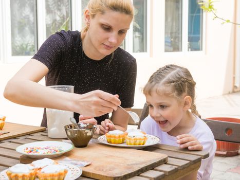 Mom puts confectionery glaze spoon on Easter cupcake, daughter happily looking
