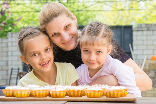 Mother hugging her daughters who cook delicious cupcakes