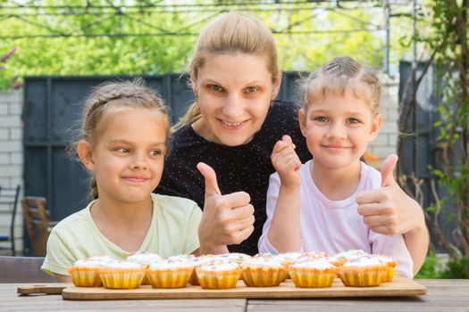Mother and two daughters show a thumbs-up, and dress easter cupcakes