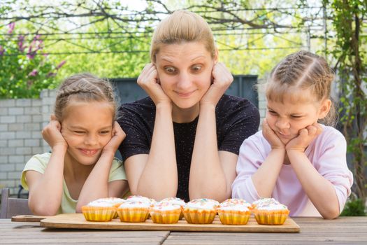 Mother and two daughters with different funny emotion looking at easter cupcakes