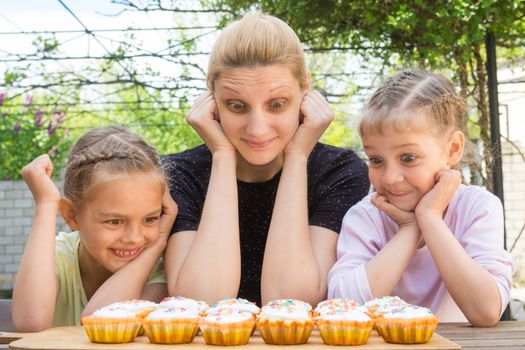 Mother and two daughters with a good appetite and big eyes looking at easter cupcakes