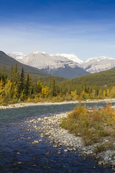 Bend of Snaring River in Jasper National Park, Alberta province, Canada.  The park is a UNESCO World Heritage site. Snow on peaks of mountains behind flowing stream. Snaring river is a tributary of Athabasca River.   