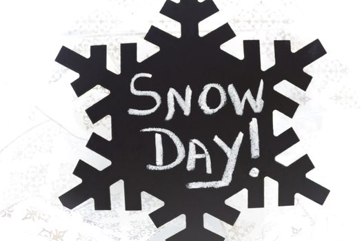 Snow Day! written in chalk on black chalkboard snowflake placed on swirl of silver, wintry ribbons.