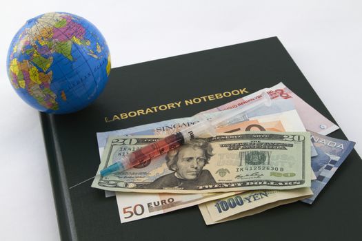 Global currency with lab syringe placed with laboratory notebook and globe reflect investment and research support of economic and social sectors including medicine, healthcare, and pharmaceuticals.  Money includes is from America, United States, Canada, China, Singapore, and Europe in forms of dollars, yen, and euro.