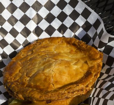 Freshly baked chicken pot pie served outdoors on black patio table. Informal presentation of comfort food, hot with oozing gravy and flaky brown crust on black and white paper. 