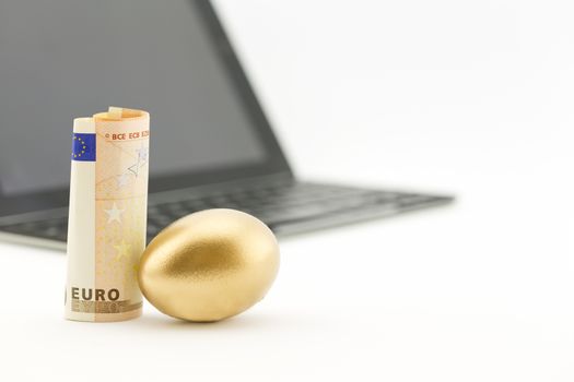 Gold nest egg next to euro currency with shallow depth of field view of technology reflects successful investing. 