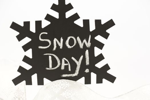 Announcement of Snow Day! written on old, dusty black snowflake against white background and with silver ribbon below. 