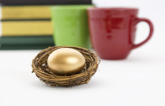 Successful, collaborative investment reflected in two coffee mugs, red and green, and books combined with selective focus on gold nest egg.  Education, due diligence. and smart, winning strategy reflected in symbols. 