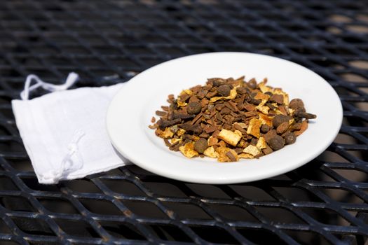 Mulling spices on white plate place on wrought iron table with small, white cloth spice bag underneath dish. Rustic, horizontal image with copy space. 