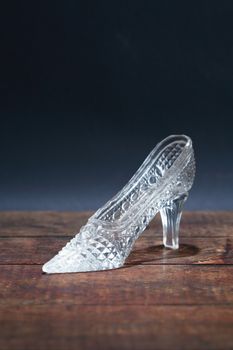 Glass slipper on old wooden board against dark background