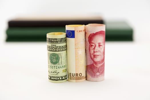 Three currencies, dollar, euro, and yen, are placed together. Selective focus on money.  Books behind on white background.  Financial issues of European Union, dollar, and yen are connected in global markets. 