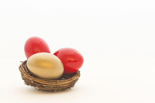 Two red eggs and one gold egg in nest reflect important choices in business and investing. Copy space on white background. 