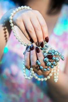 beautiful hand of a young woman with brown manicure holding white pearl necklace