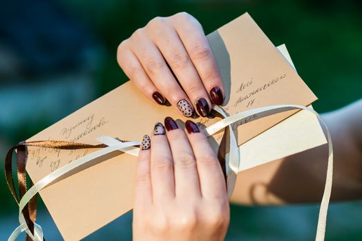 Beautiful hand of a young woman with brown manicure holding an mail envelope isolated