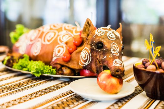 Decorated and roast suckling pig with an apple in his mouth on a white plate on banquet