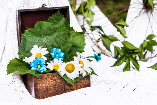 old brown box decorated with camomiles and fresh leaves in a white tablecloth