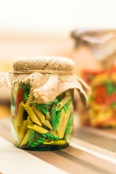 Dry colored pasta in a glass jar on the table