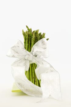 Vertical photo of asparagus stalks tied with white ribbon.  Still life with white background and copy space. 