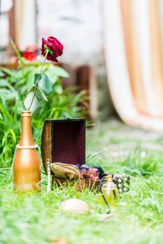 Red Rose in a gilded bottle at the open boxes on the green grass