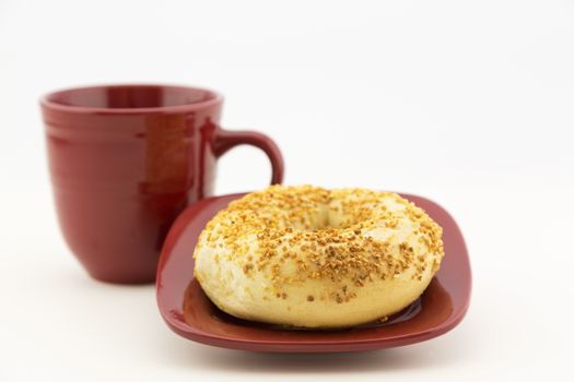 Fresh garlic bagel on square red plate with matching mug.  Horizontal food image with copy space. 