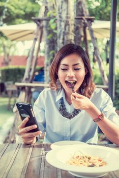 Asian women are happy when eating and playing mobile games,focus on the face.